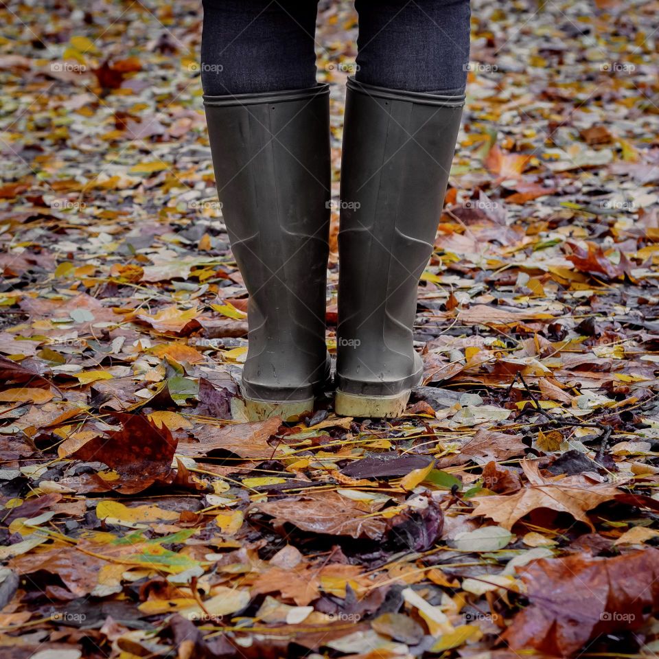 A person wearing green Wellington boots stands on wet, fallen leaves in autumnal tones