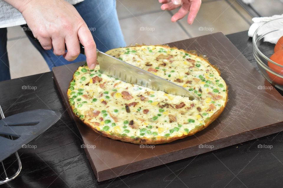 Homecooking cooking Frittata at home and adding and mixing ingredients and removing the Frittata from the pan for cutting and serving on a white plate with tomatoes. Healthy home cooking in kitchen. Breakfast and lunch food preparation.