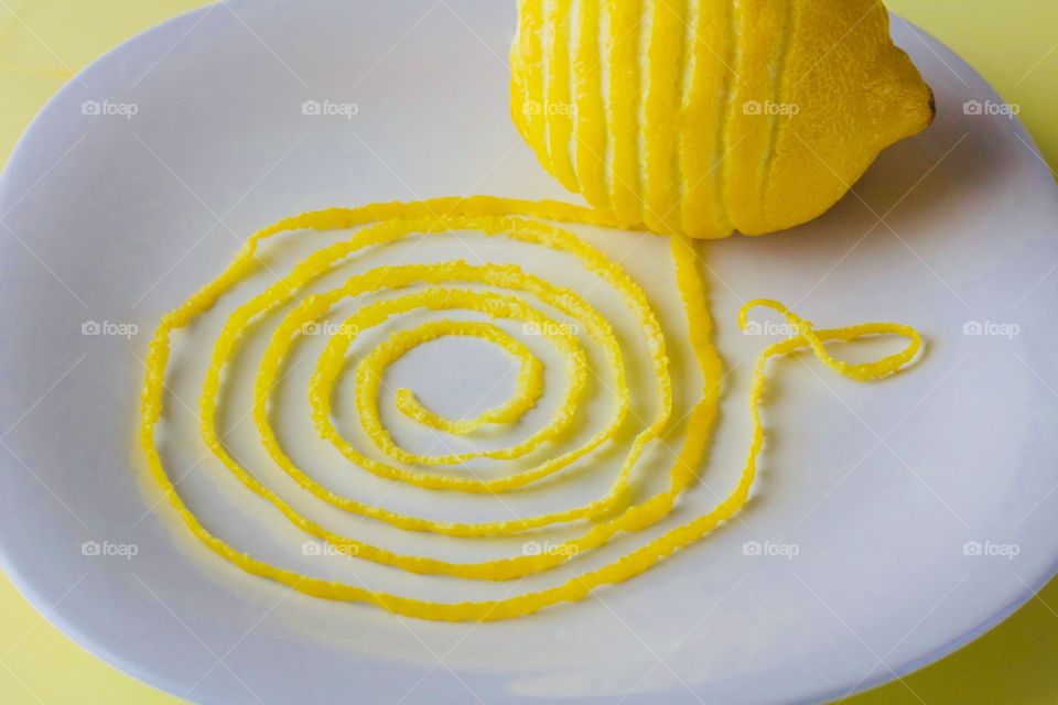 Lemon and spiraled lemon peel on a white plate with yellow background  