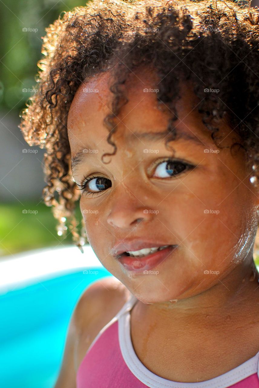 Cute little girl enjoying some playtime in a swimming pool during a hot summer day, looking for refreshment