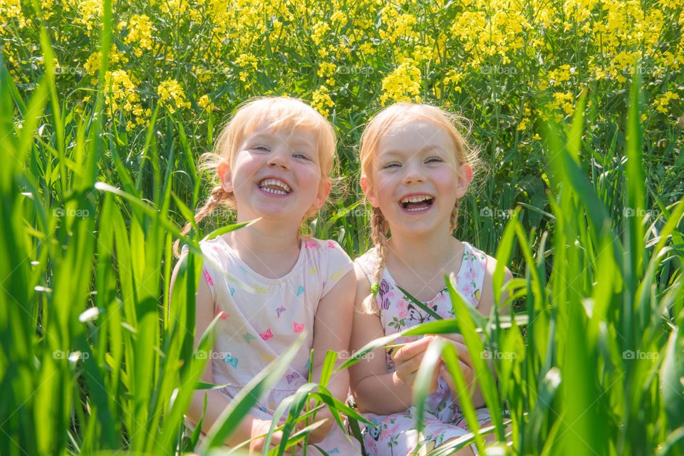 Blonde cute girls sitting in field laughing
