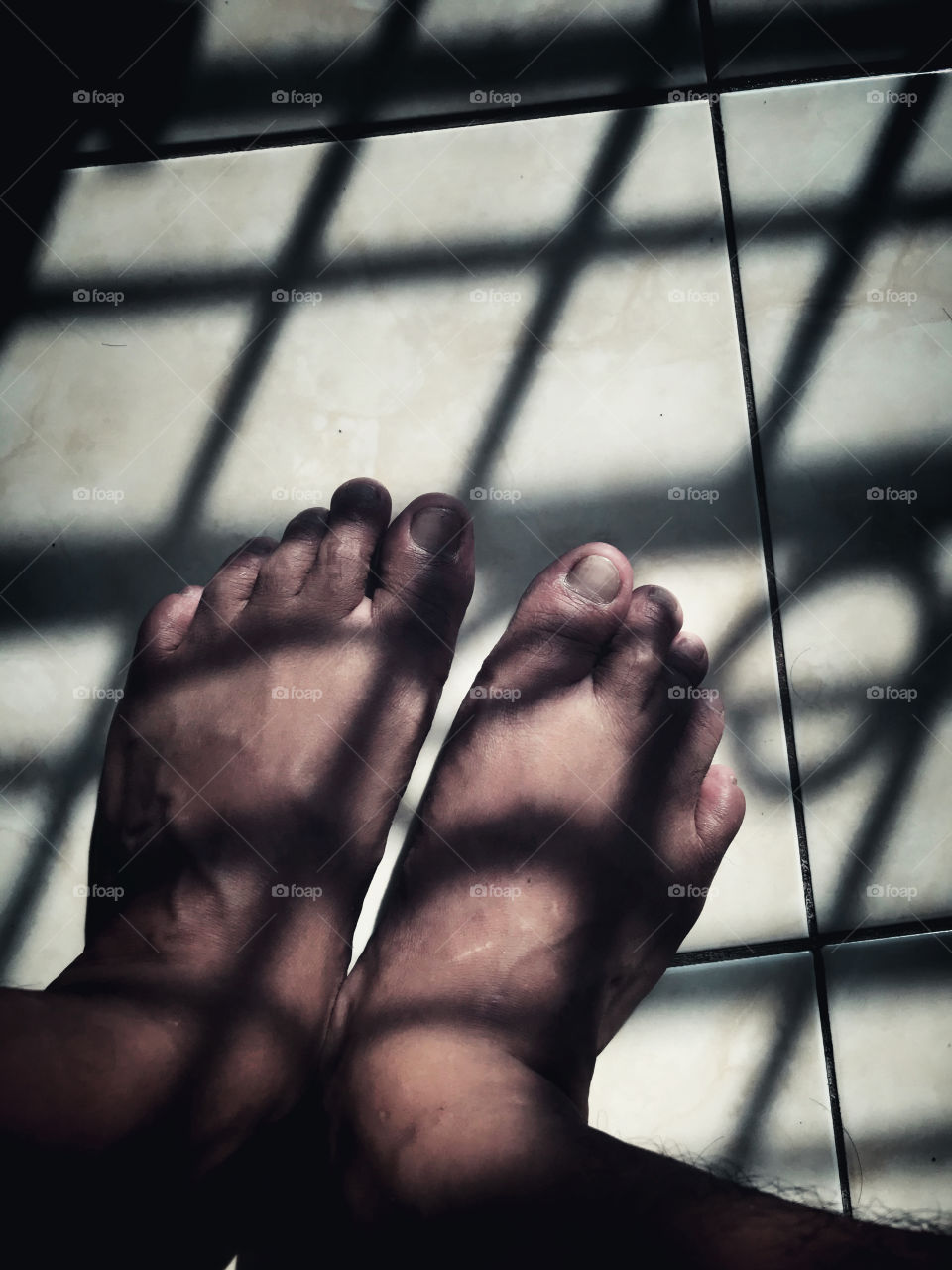 Middle age man feet, shot during perfect sunset light inside the room with the shadow of an iron window’s fence