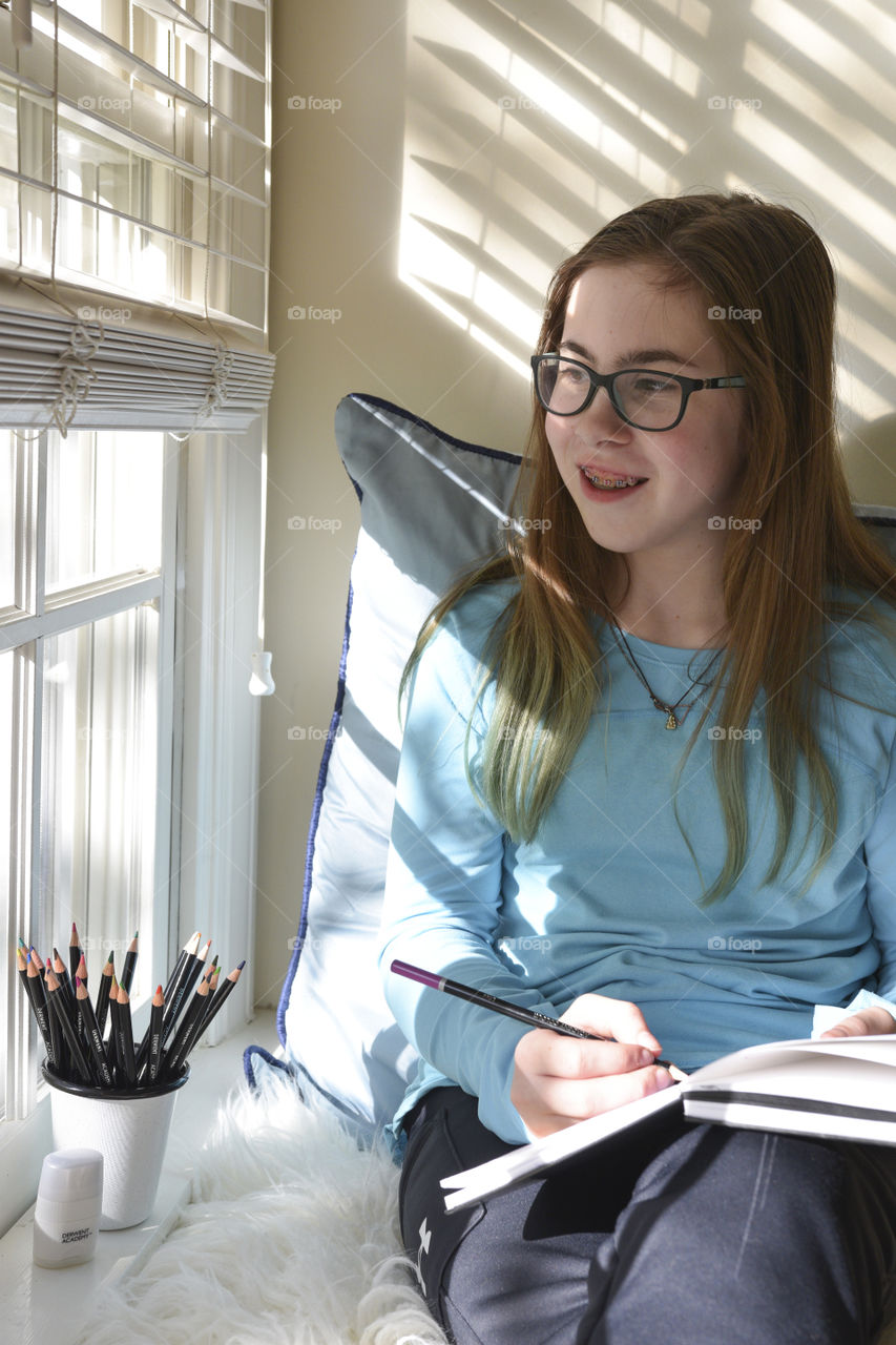 Girl with Art Supplies in a Window Seat at Home