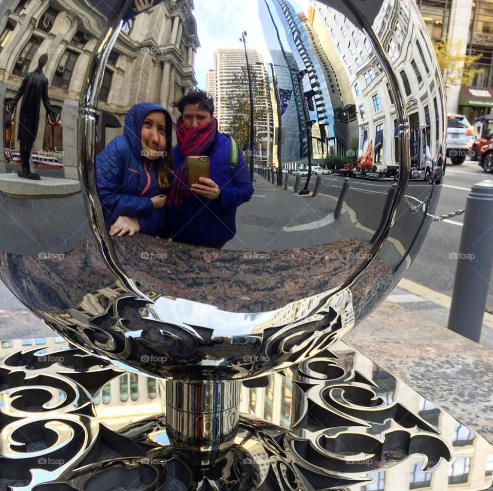 Distorted reflection of people in a mirrored sculpture in the city 