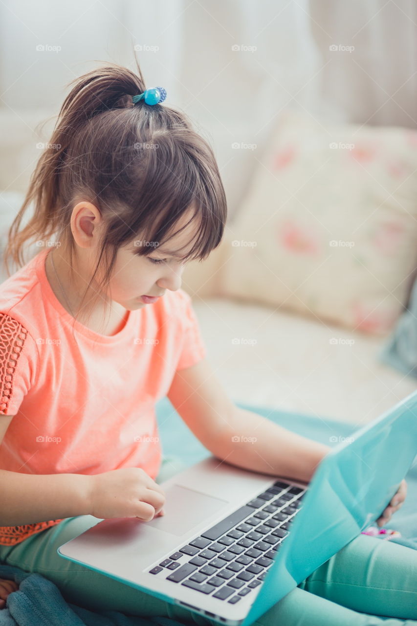 Little girl with gadgets(laptop and tablet) in the bed.