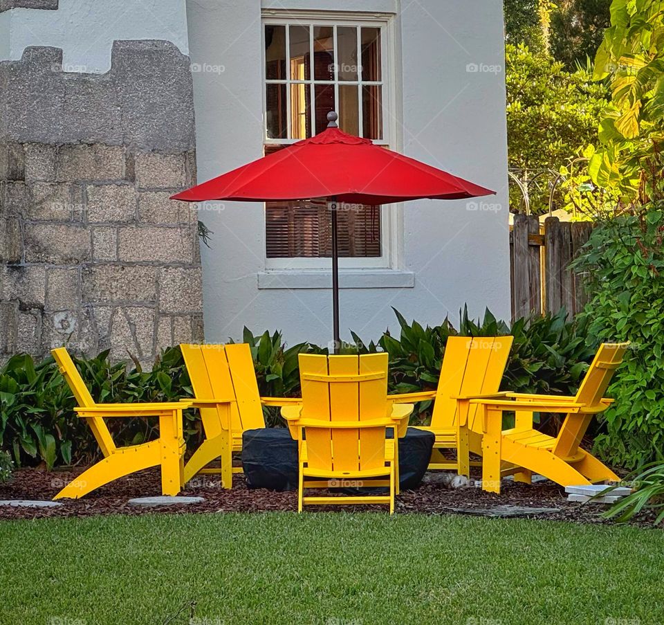 Yellow Adirondack chairs under a red umbrella 