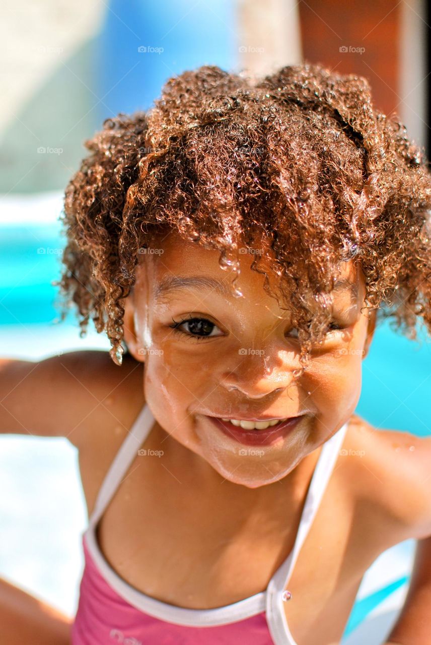 Cute little girl enjoying some playtime in a swimming pool during a hot summer day, looking for refreshment