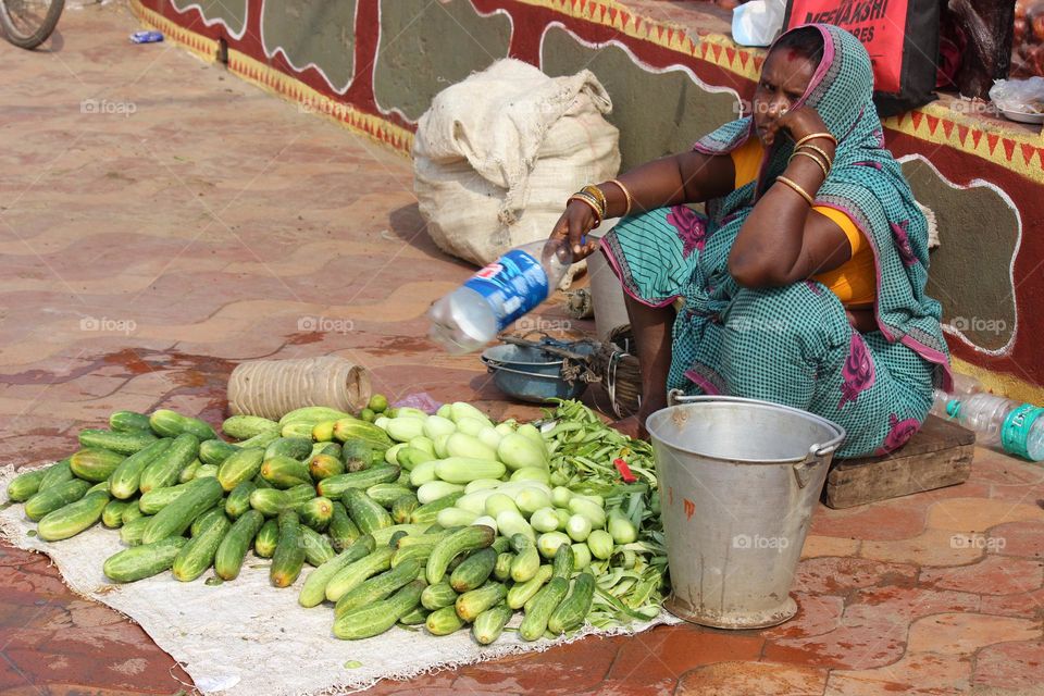 This picture was described about a lady selling cucumbers over the beach and waiting for the customers.