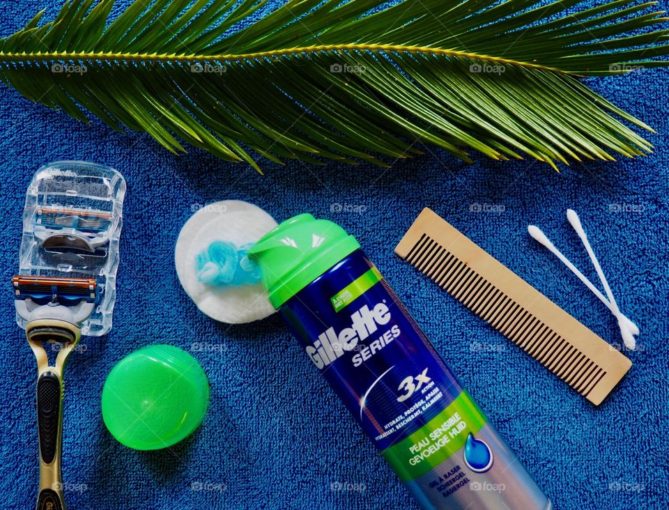 Gillette shaving cream and razor on a blue towel with comb and palm leaf 