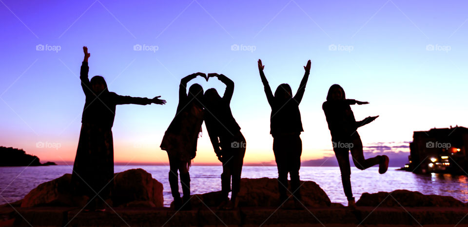 Silhouette of people making love sign by sea during sunset