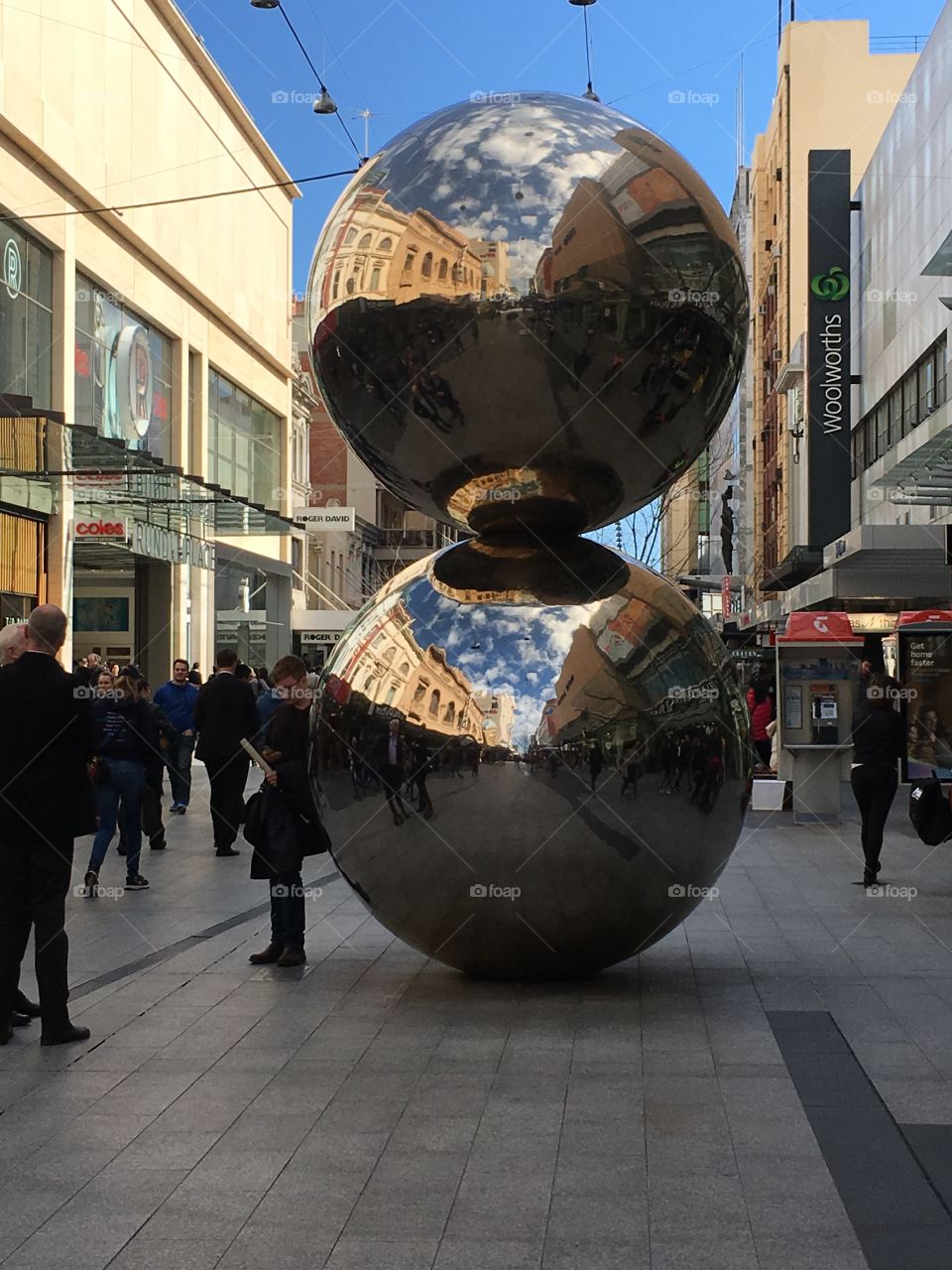 A striking large silver sculpture in downtown Adelaide south Australia reflecting building s, people, and vendors 