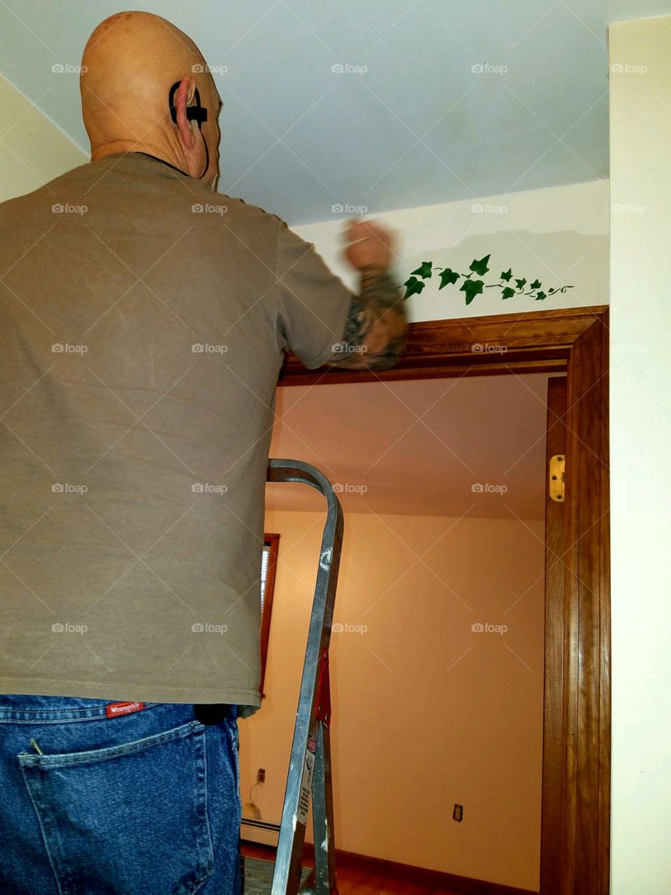 Remodeling house with painting walls & painting over doorway using hand brush while standing on ladder.