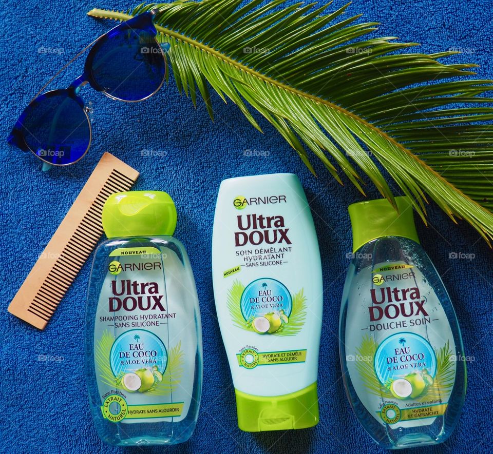 Garnier shampoo, conditioner and bath gel on a blue towel with comb and palm leaf and blue sunglasses.