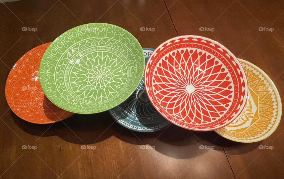 The five bowls, stacked neatly on display, showcase a striking array of vibrant colors and intricate designs. Each bowl is uniquely colored and the designs vary as well. The display creates a stunning visual contrast, and playful yet artistic nature.
