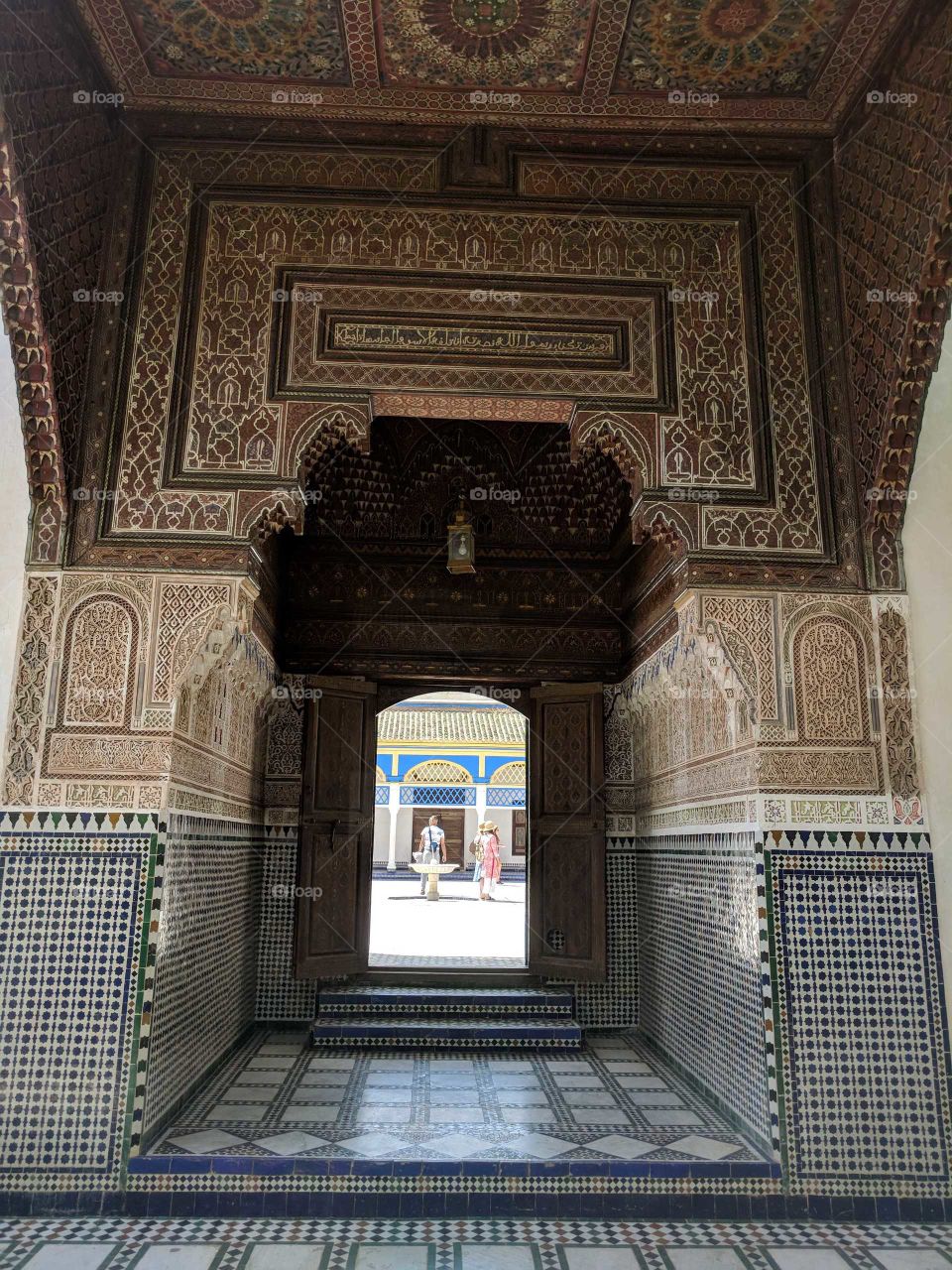 Gorgeous Ornate Ceramic Tile Mosaic Entrance (Doorway) Looking Out Over a Courtyard and Two People in the Bahia Palace in Marrakech in Morocco