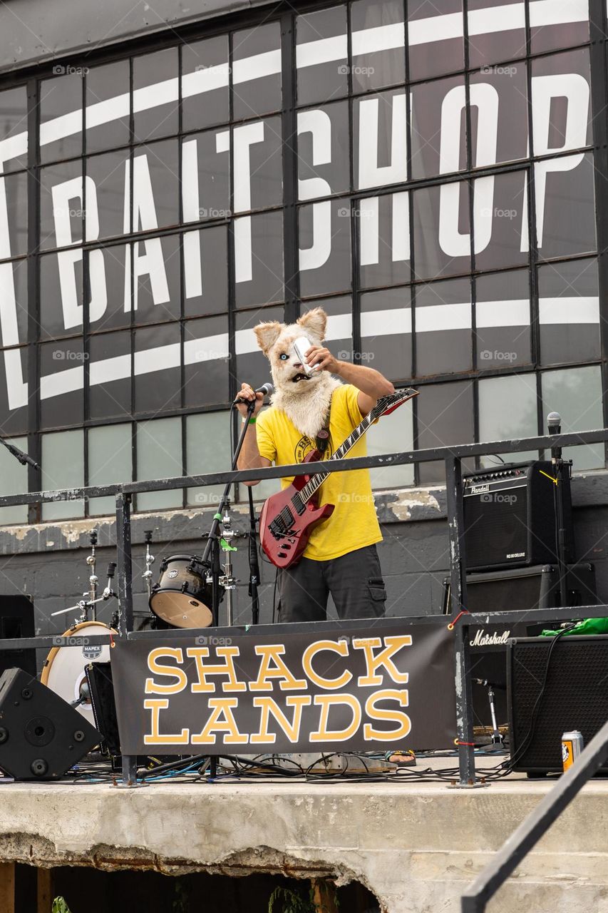 Guitarist wearing a cat mask drinking a beer on stage at a concert