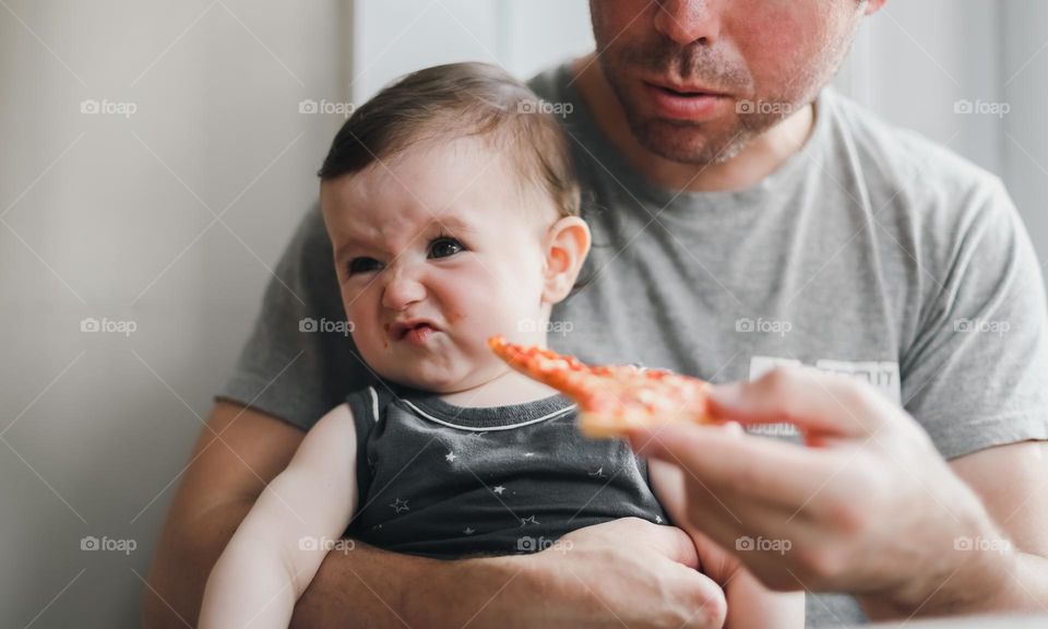 Caucasian dad hands feed his little daughter in his arms with a piece of homemade poultry, and the child wrinkles his face without eating, close-up side view. The concept of fathers, feeding the child, at home, home sweet home, family happiness.