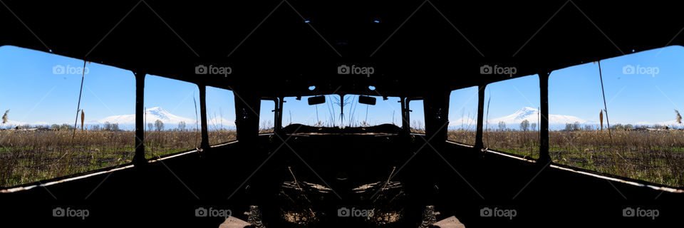 View from inside of an abandoned and rusty old Soviet Russian bus in the middle of reeds and agriculture fields with snow-capped scenic Ararat mountain and clear blue sky on the background in rural Southern Armenia in Ararat province on 4 April 2017.