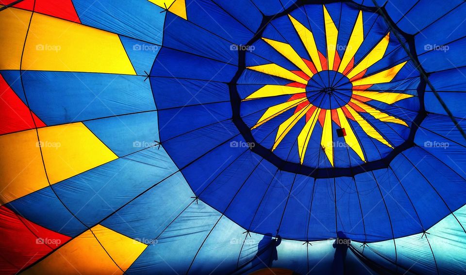 Setting up a giant, bold, geometric, colorful and beautiful hot air balloon viewed from the inside  with the silhouette of two people helping setting it up.