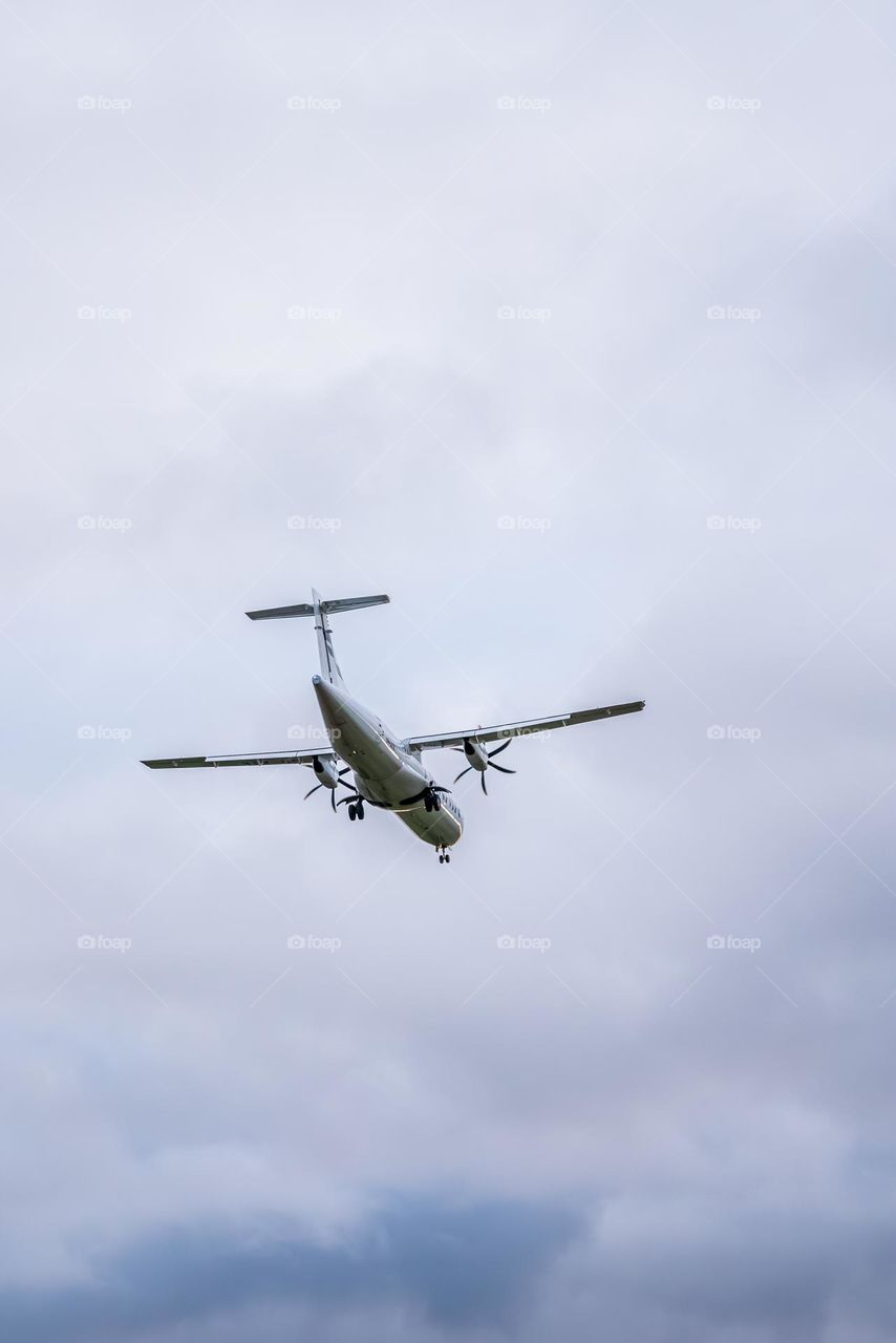 an airplane files through a cloudy sky with a red tail light