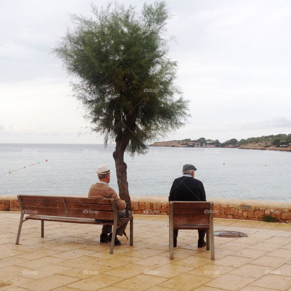 2 elderly man sitting on the bench & watching the sea