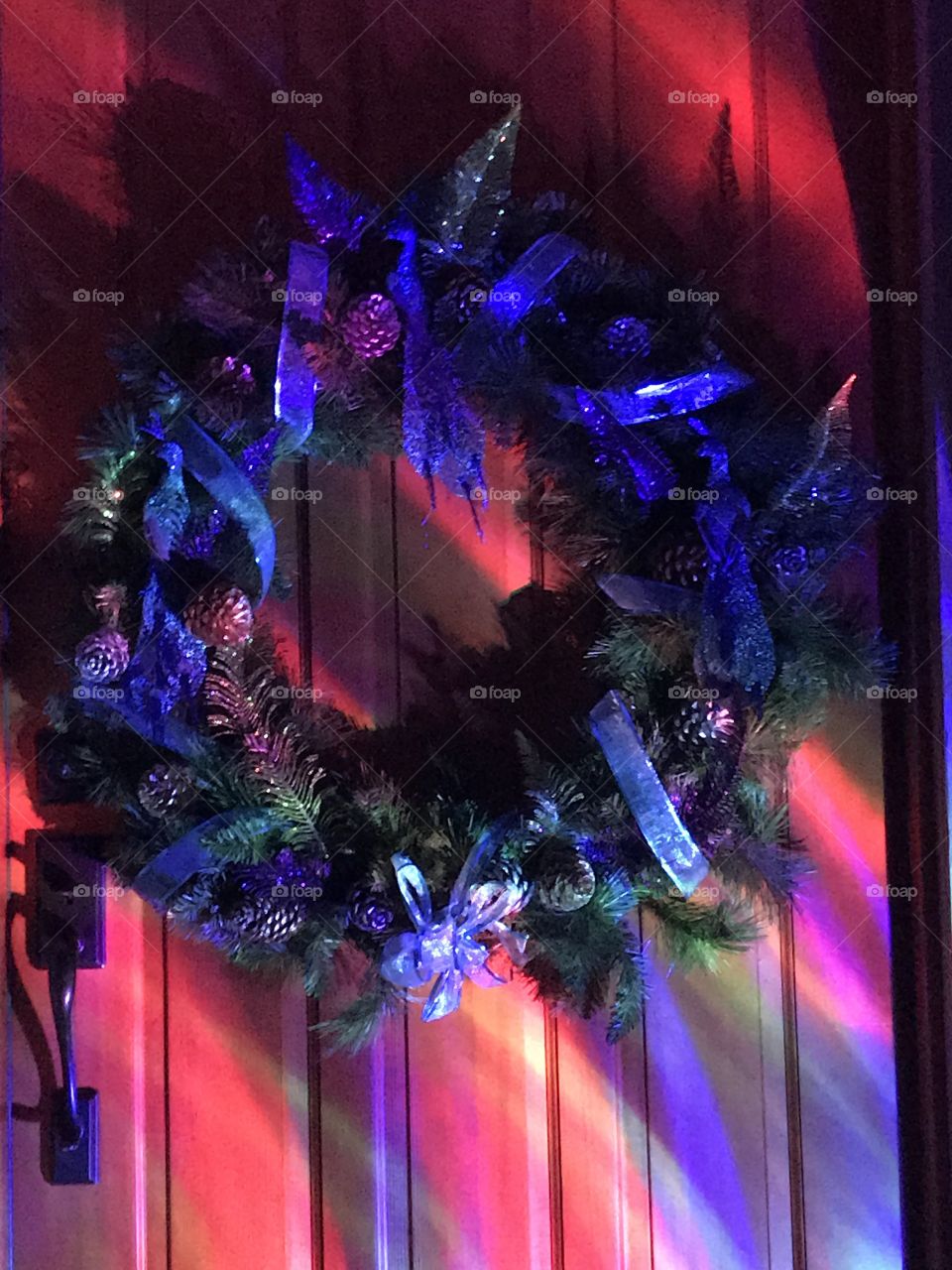 A nighttime shot of the Christmas wreath on my front door with the pink, blue and purple tones of my led projector light shining on the wood door.