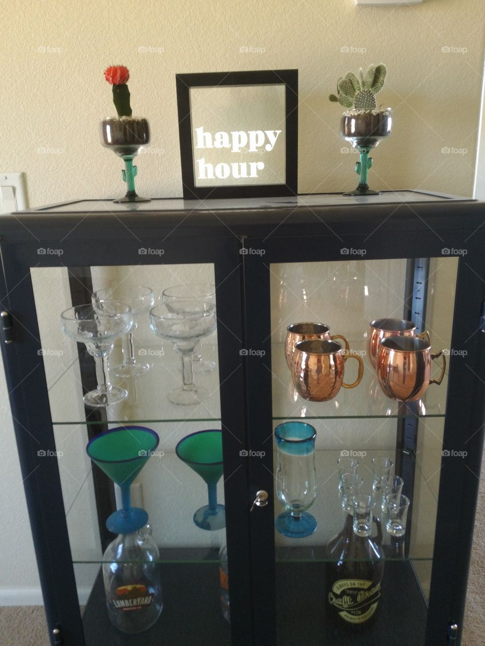 happy hour signed setting on bar with cactus in margarita cup and other bar glasses