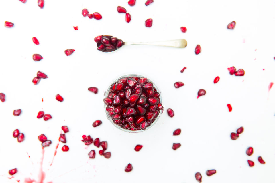 Fresh red pomegranate lay flat with seeds in a bowl and scattered pomegranate seeds and a spoon. Lay flat on white background. Fresh and juicy display of pomegranates.