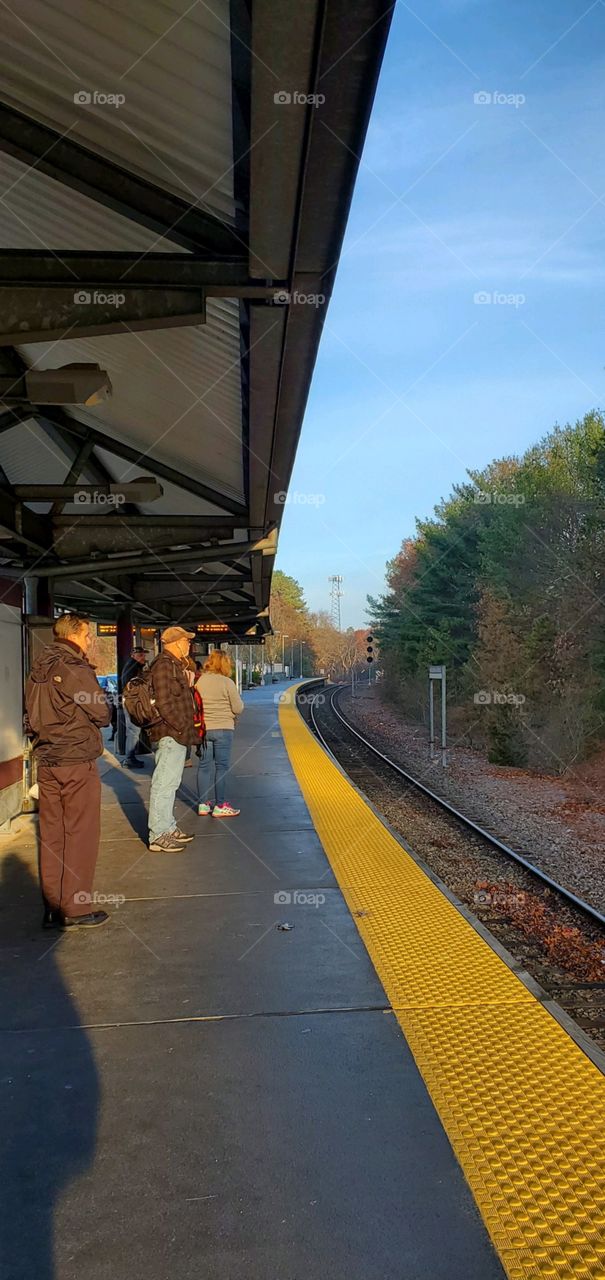 Passengers waiting on platform for next train commuting to work or pleasure trip. Clear day with blue sky but cold out waiting for trains.
