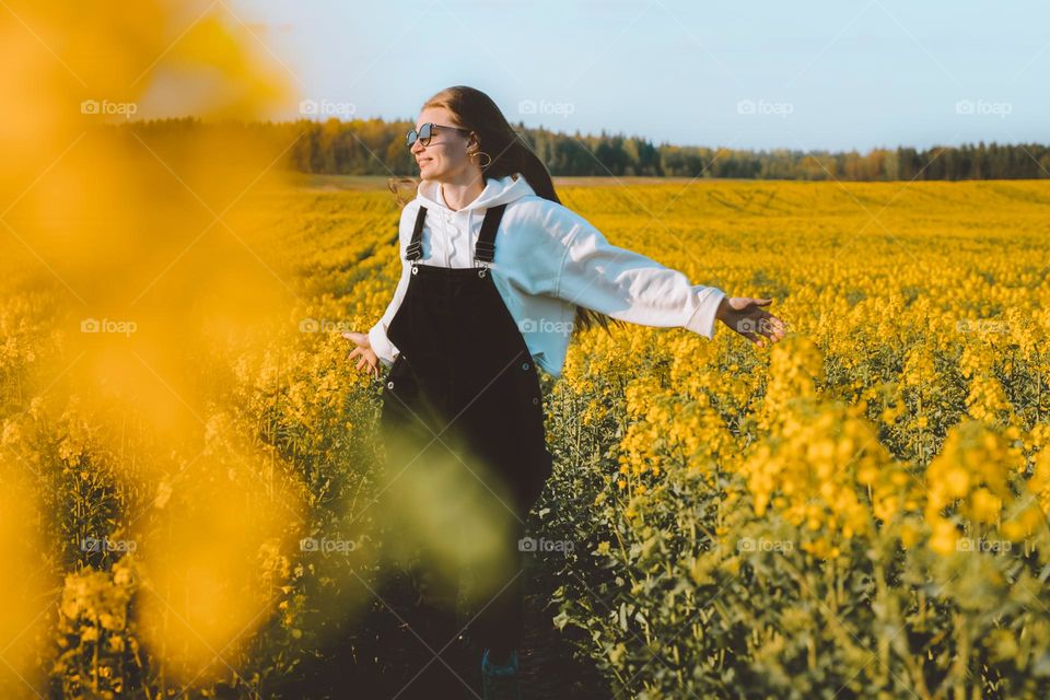 Happy young smiling woman running through the rapsfield with open wide hands 