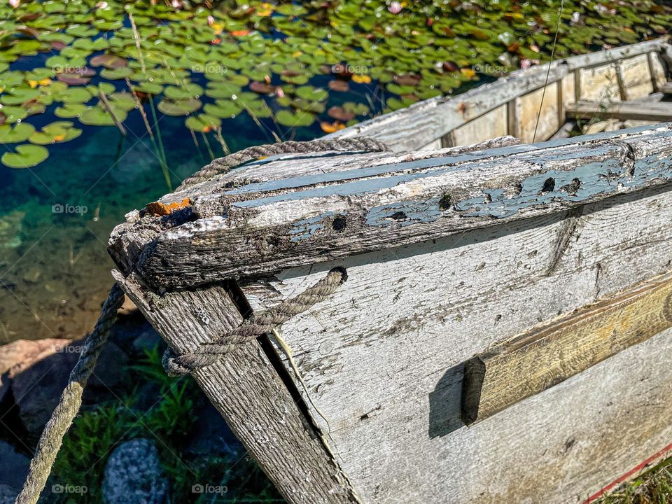 “Tethered and Weathered.”  The prow of a dory that has seen far better days sits at the edge of a pond.