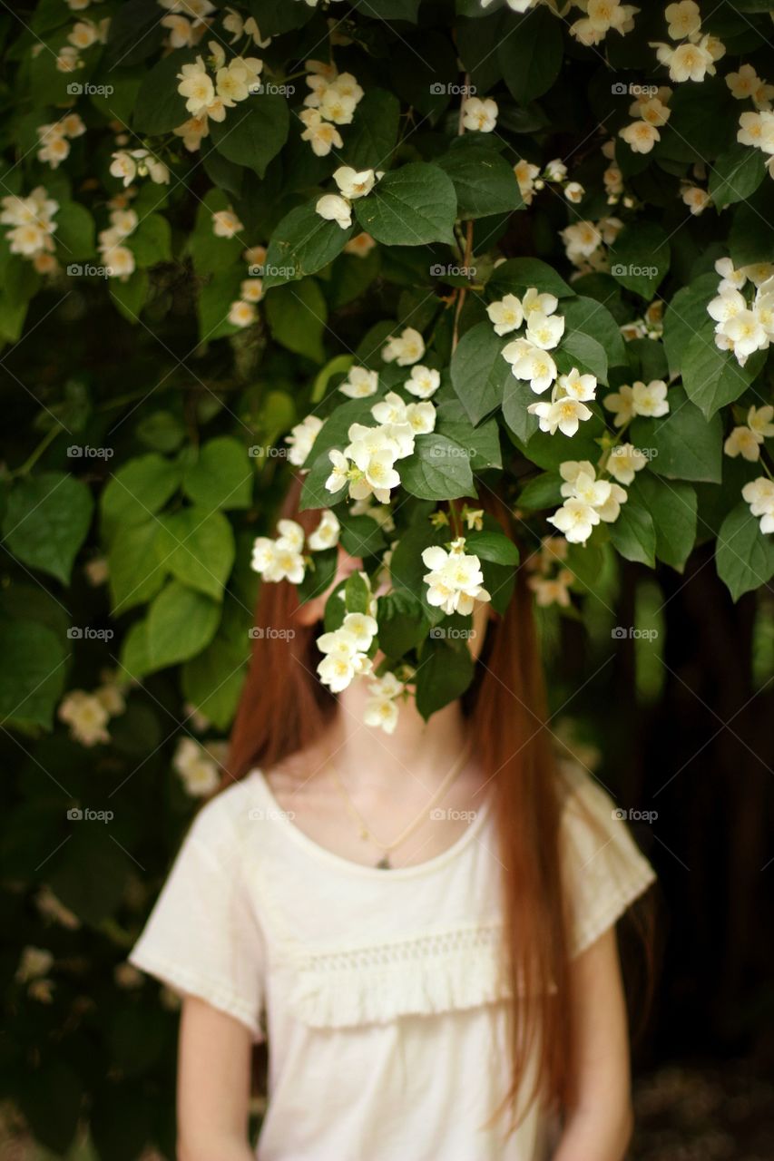 Girl with long hair in a white blouse sniffs jasmine flowers