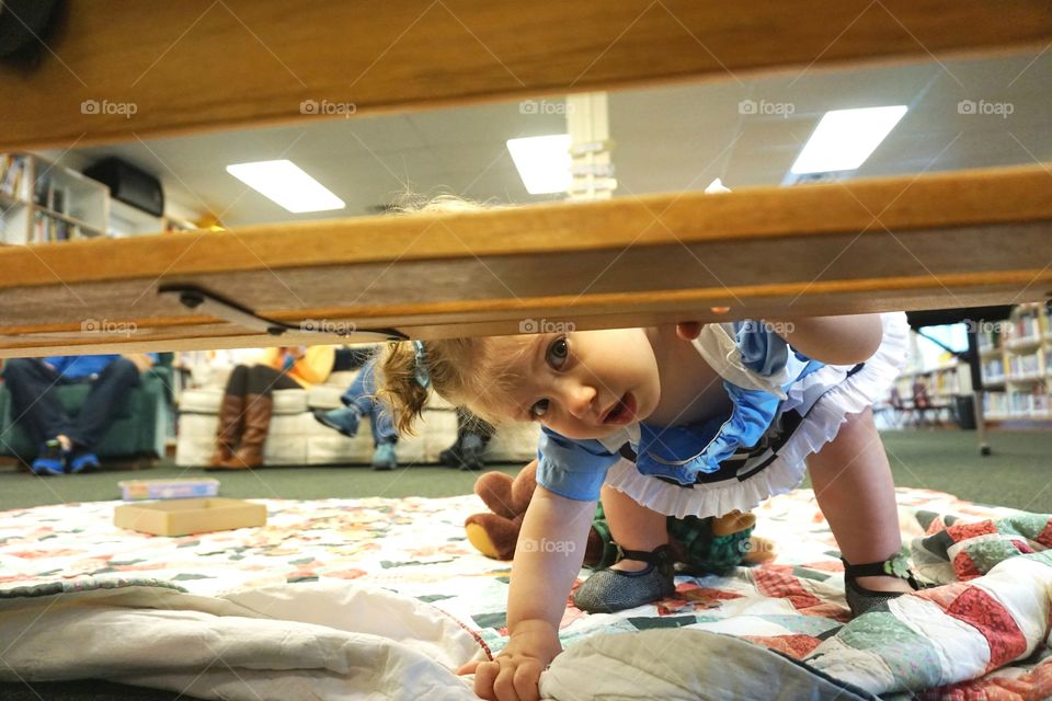 Baby girl peeking behind table at home