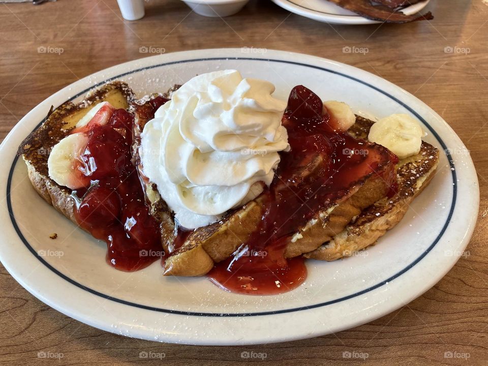 This food picture was taken on my iPhone 12, at a restaurant, in Calgary, Alberta, Canada, of my delicious breakfast of French Toast with strawberry sauce, bananas, with whipped cream and sprinkled with icing sugar….nummy!