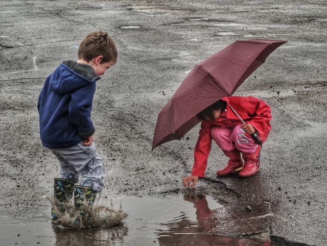 Umbrella Fun In The Rain. Young Boy And Girl Playing In Rain Puddles
