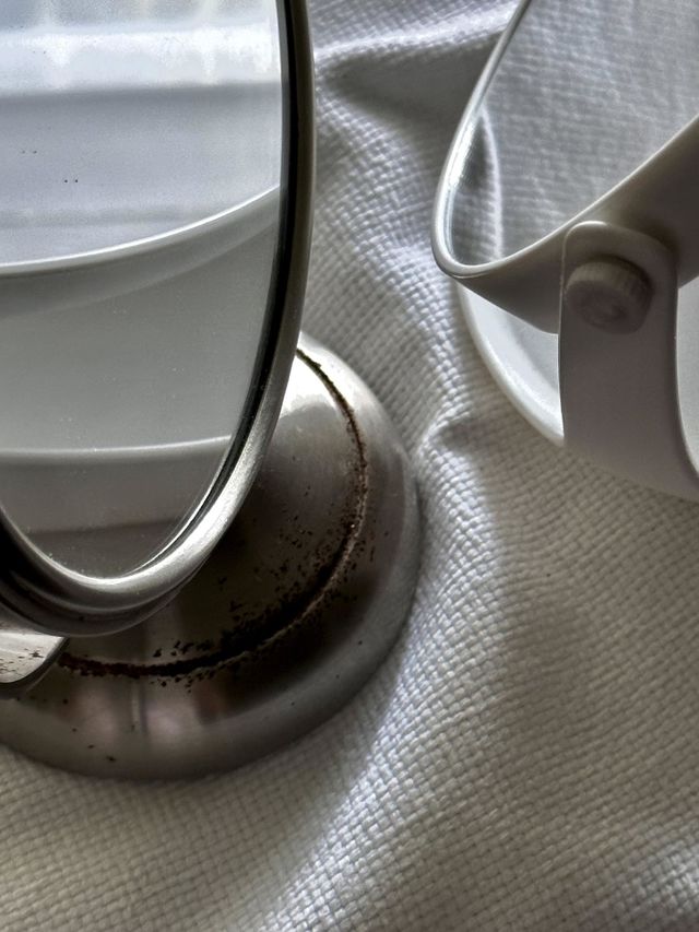 White plastic framed standing mirror reflected in vintage stainless steel double sided mirror on white cotton woven fabric