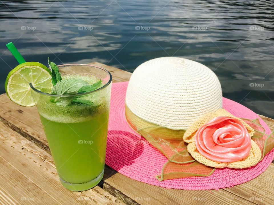 Mint lemonade glass and summer pink hat near the lake