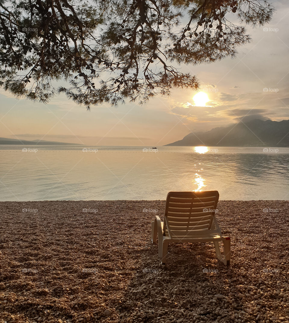 Beach chair on a pebble beach against the background of a calm clean sea, mountains and sunset.  Summer vacation at sea.  Relax
