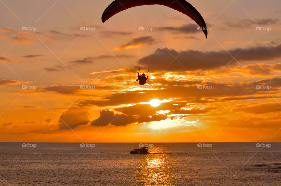 Sunset on Tenerife coast with paragliding and tourist boat.