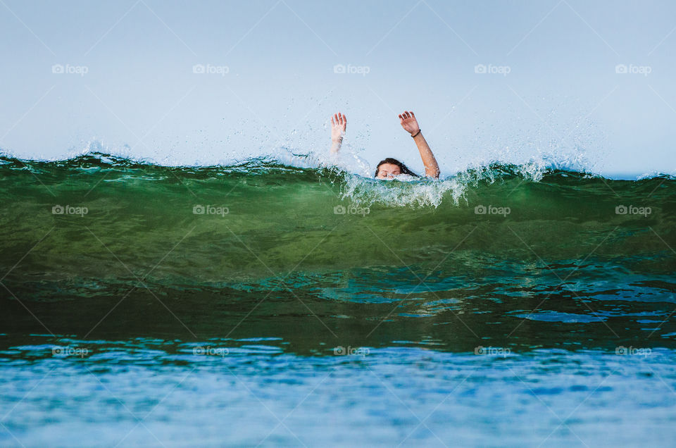 Woman with raised arms covered by the wave of the sea against the clear sky.