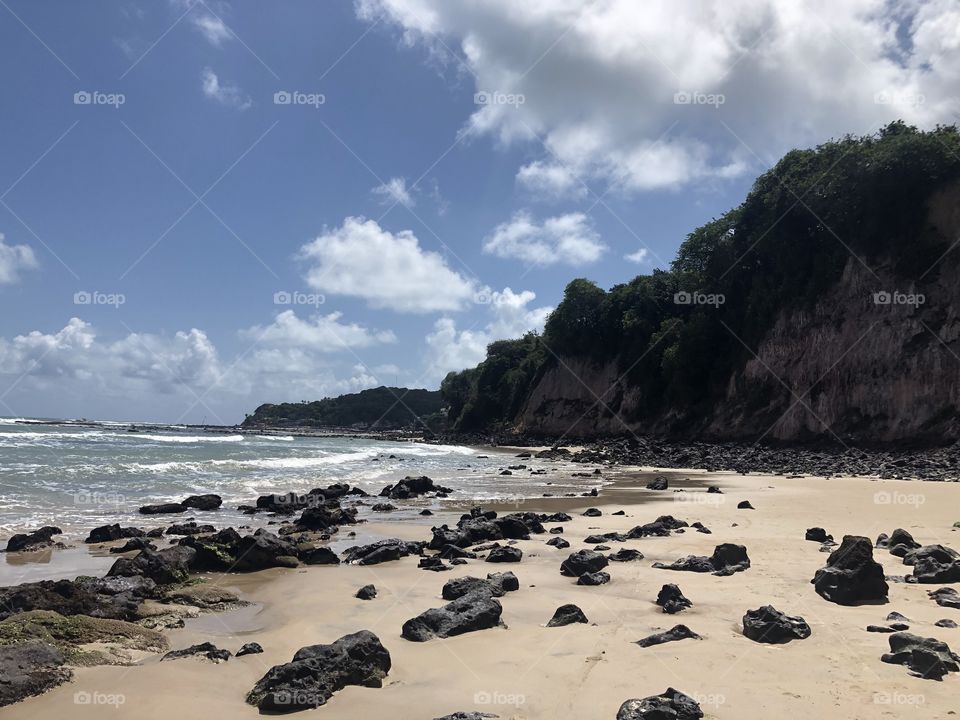 Brazilian beach covered by rocks and surrounded by a cliff