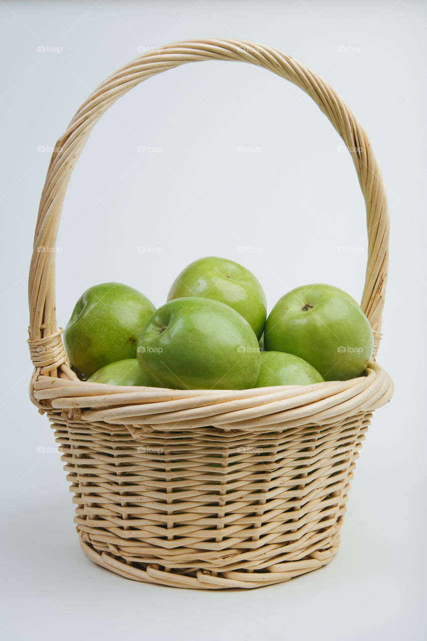 Green apples in white woven basket on white background