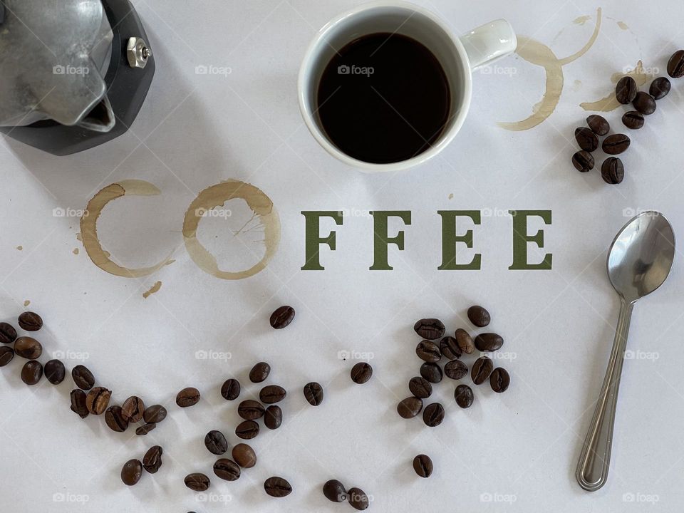 composition game of the word coffee with the imprint stamp of a coffee cup, and coffee pot and beams on white surface, coffee theme flat lay; coffee items composition