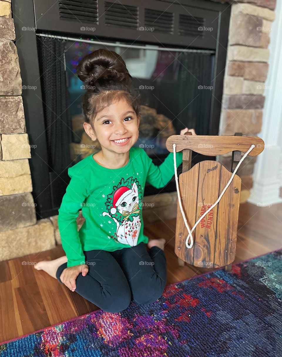 Little girl poses with sled, yearly tradition with Christmas sled, making traditions with family, wooden sleds and fireplaces