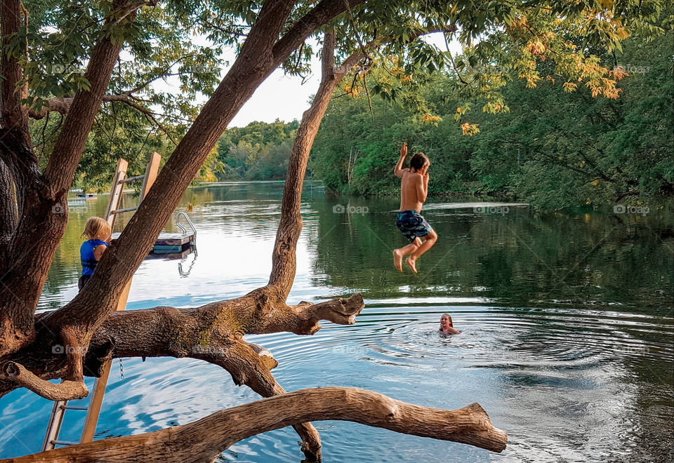 Boy jumping into lake from a tree, mid-air, summertime in the country.