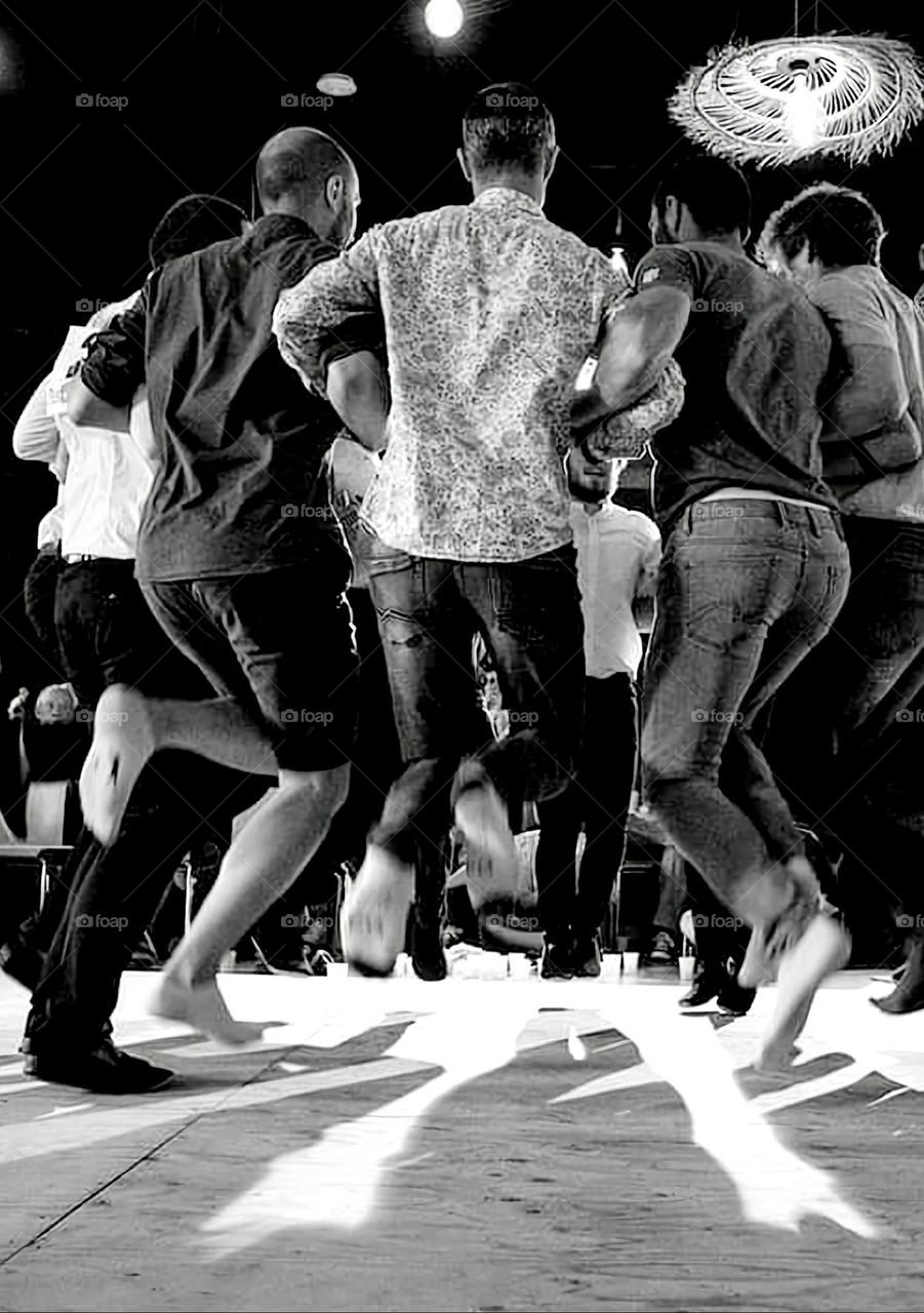 Black & white shot of the back of a group of men dancing and jumping at the Fisel dance competition in Rostrenen