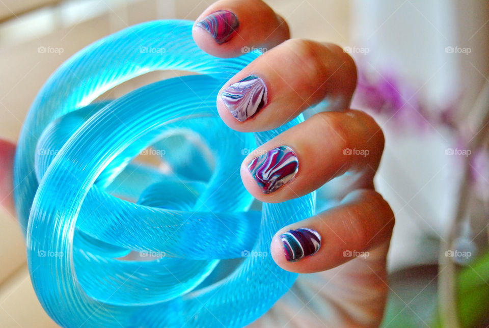 water marble nail art in purple, magenta, bluegreen and white. holding an abstract ball of art.