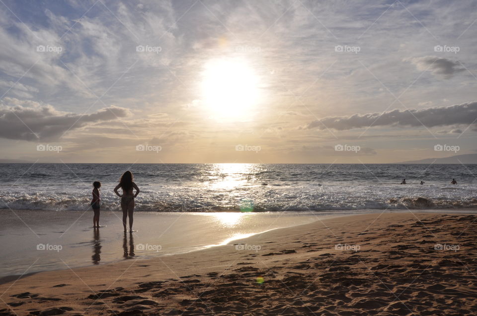 Two girls watching golden Maui sunset. 