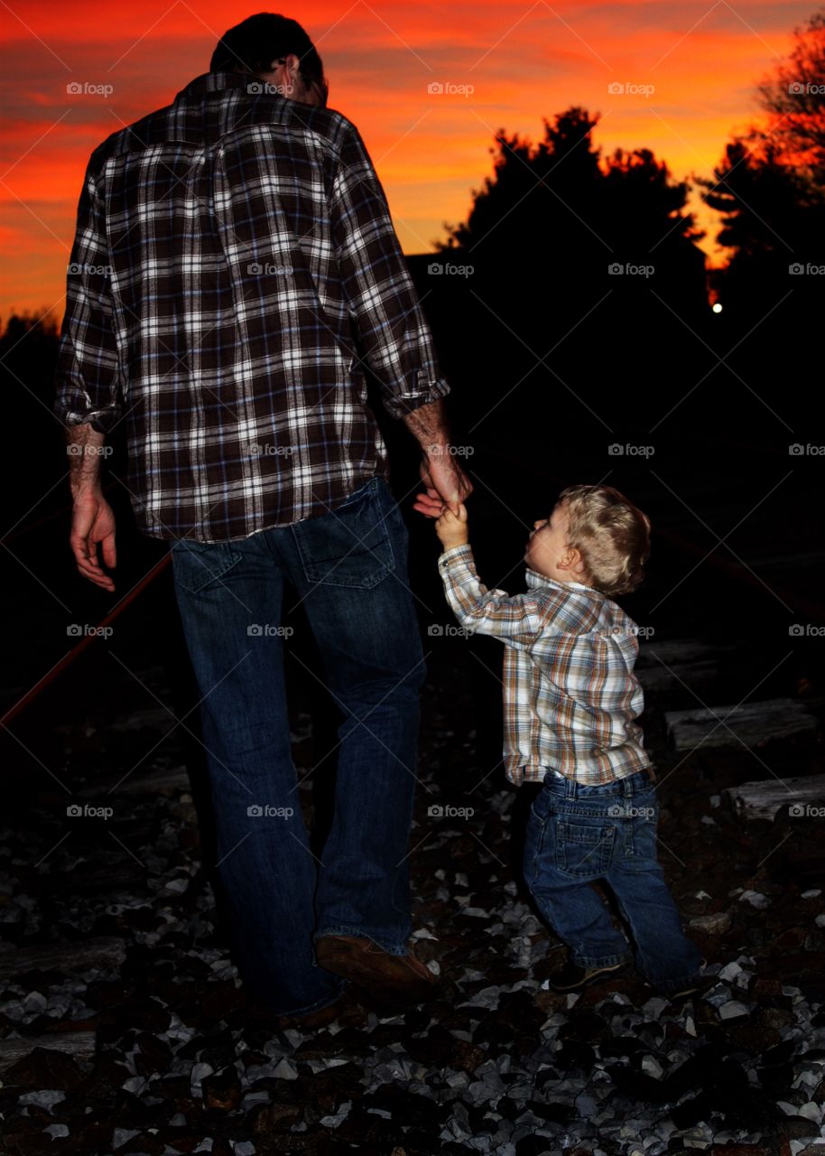 Father and son walking on empty rail track during sunset