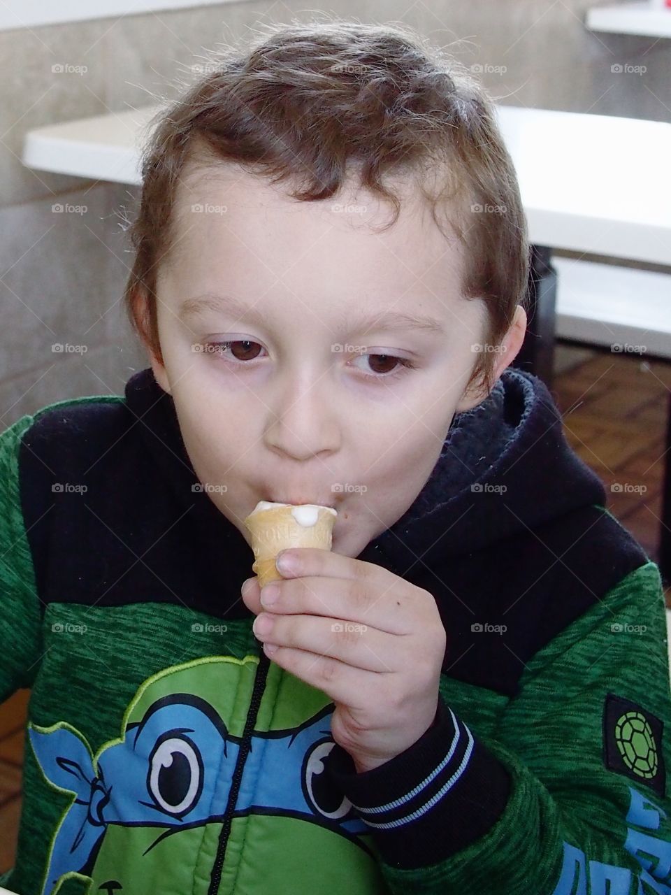 A little boy eating his vanilla ice cream cone for dessert. 